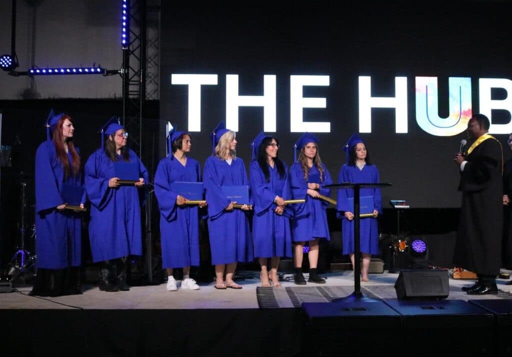 UMI graduates in blue gowns gathered on stage at The HUB
